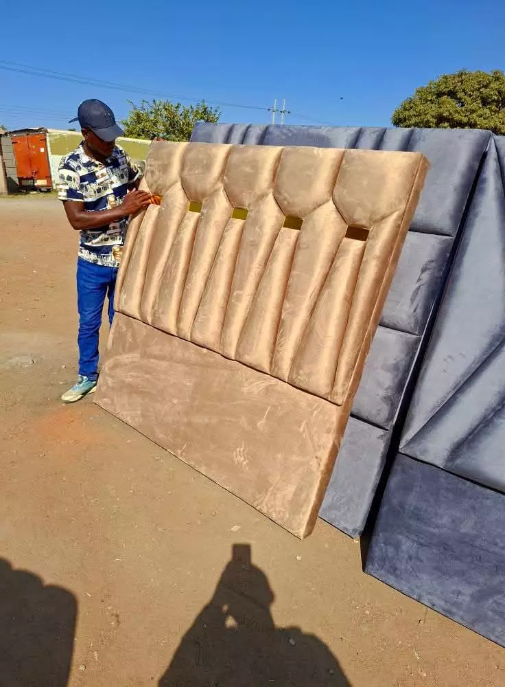 Man standing next to a large beige tufted headboard with grey headboards stacked behind