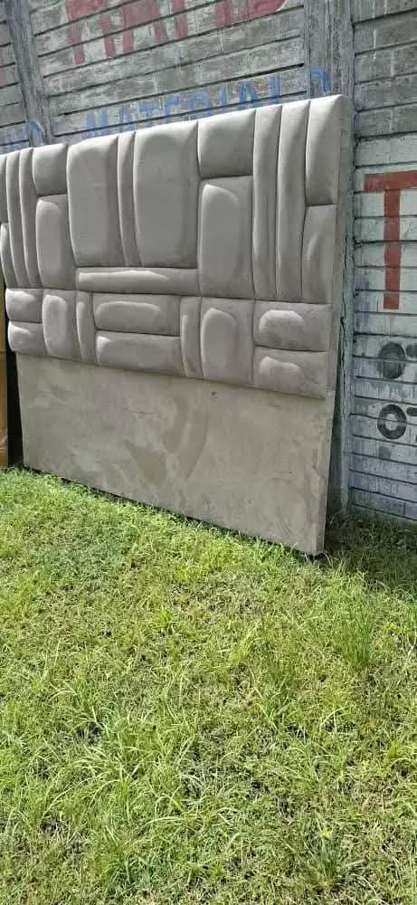 Upholstered headboard standing on grass against a painted brick wall