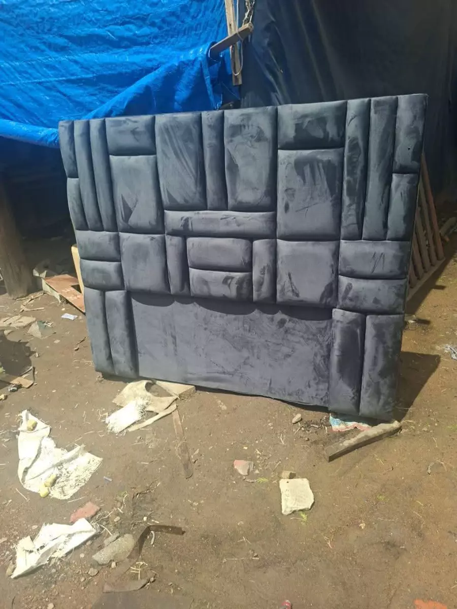 Geometric upholstered headboard resting on dirt ground in an outdoor workshop